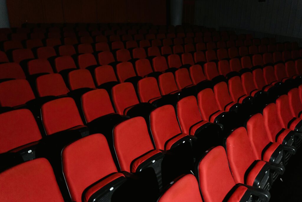 A view of empty red theater seats arranged in rows inside a cinema hall.